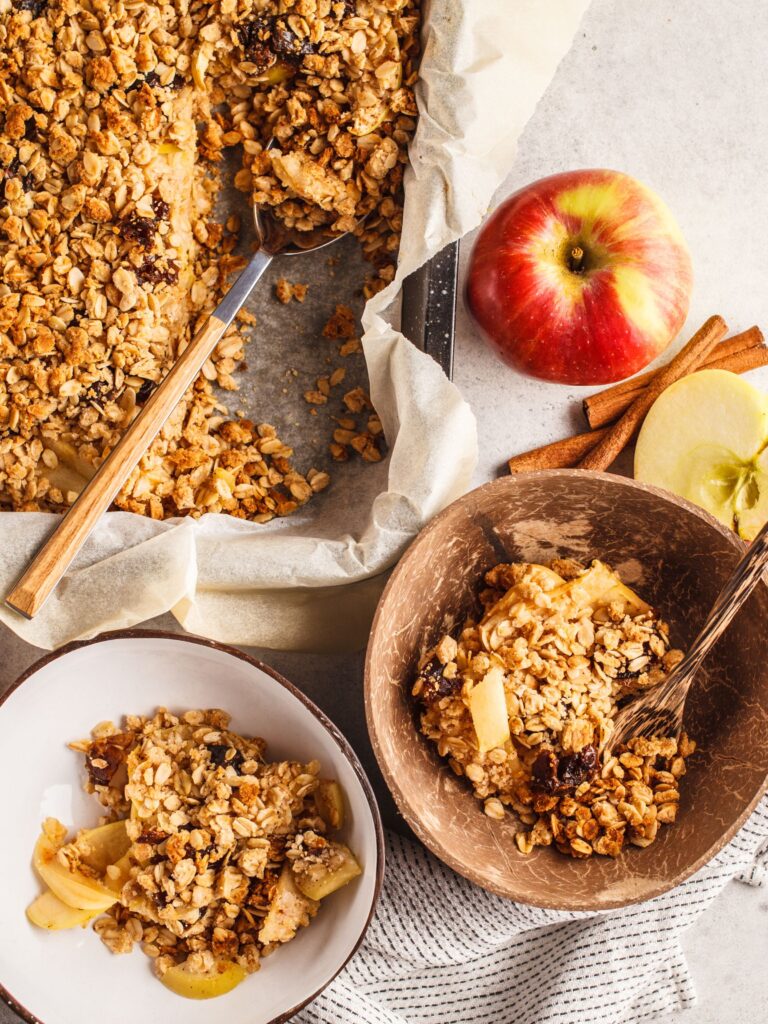 a tray of apple crisp, 2 bowls of apple crisp and an apple sitting on a table