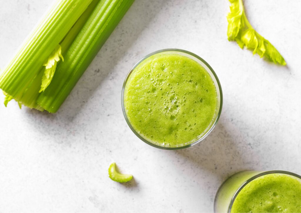 green juice sitting on white countertop next to celery stalk