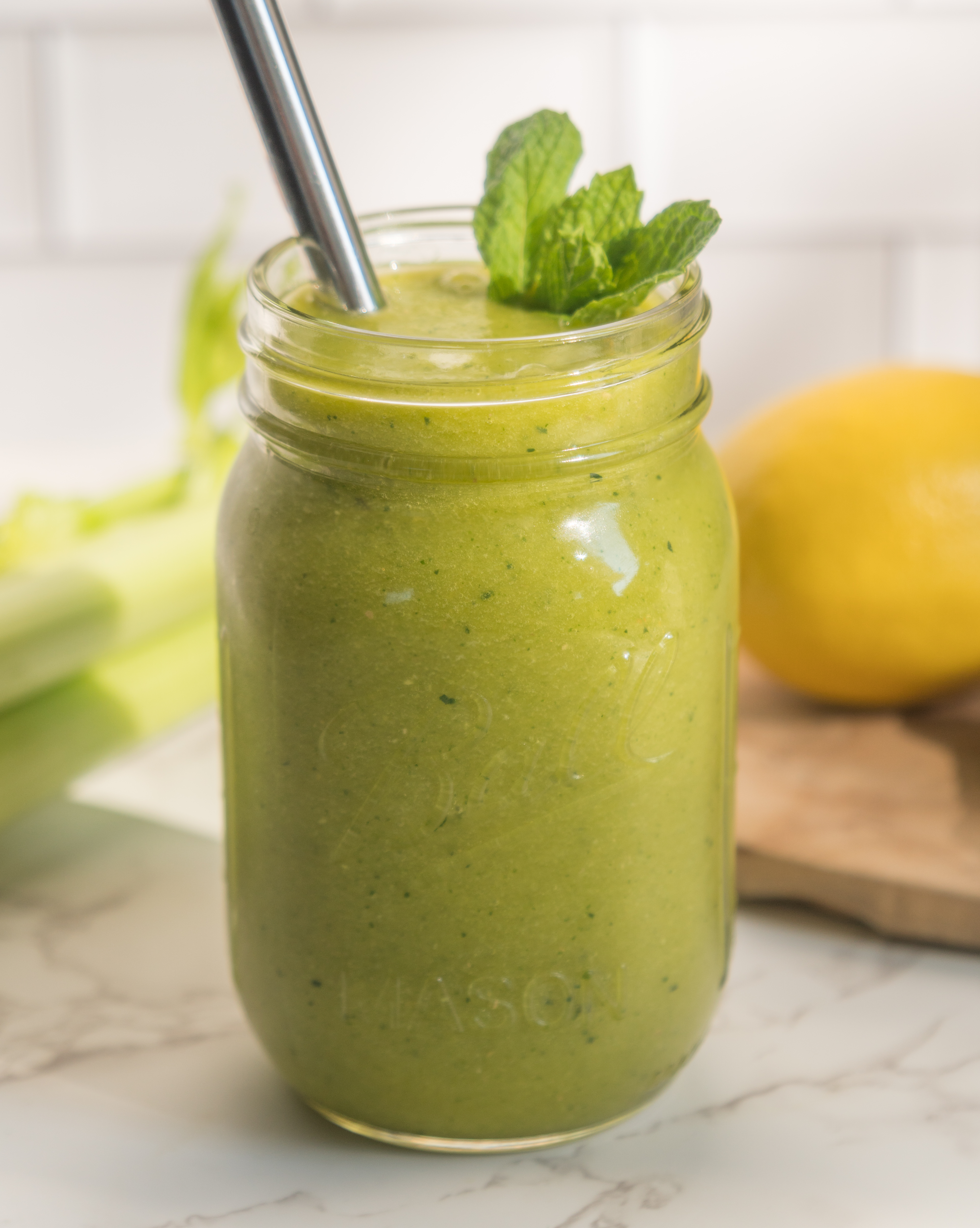 green smoothie in mason jar in front of lemon on cutting board