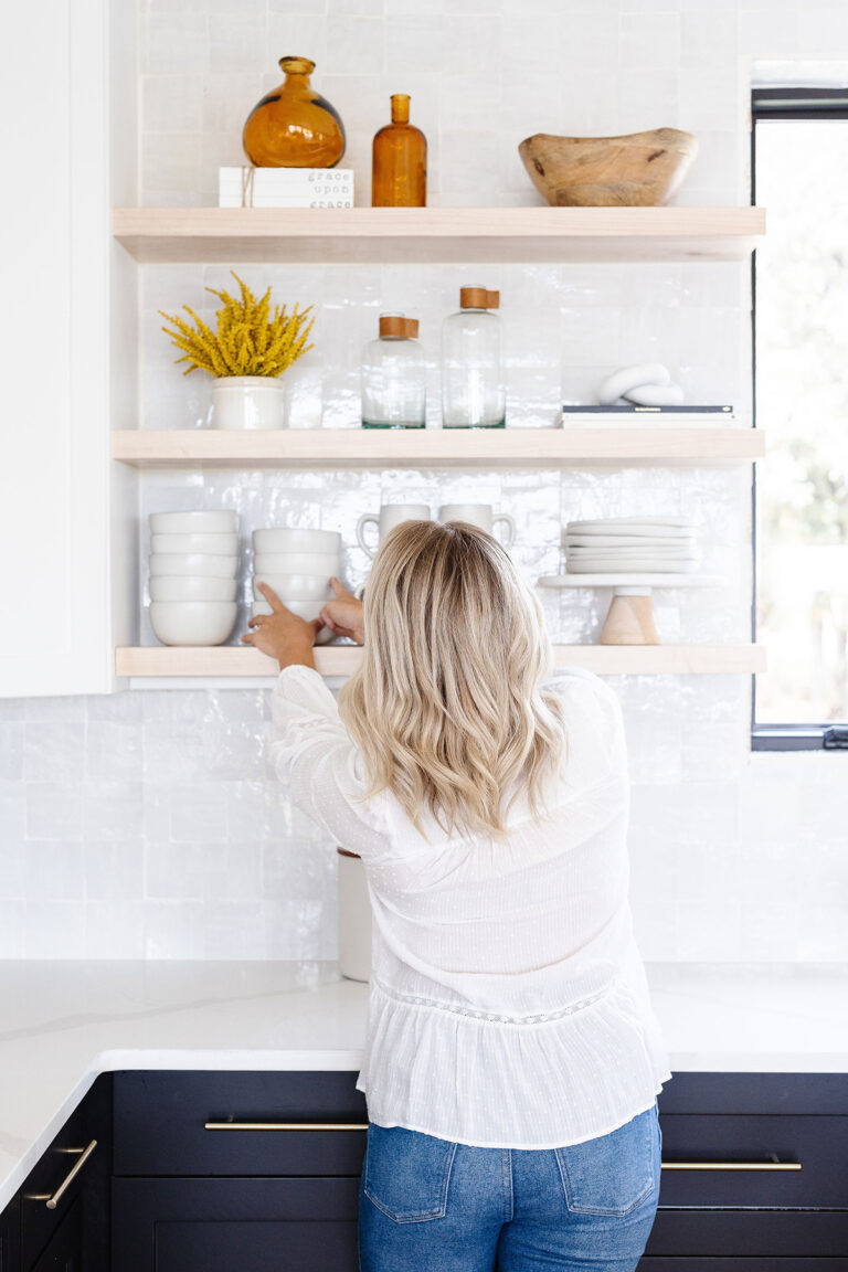 A lady placing white bowls on a shelf in a white kitchen