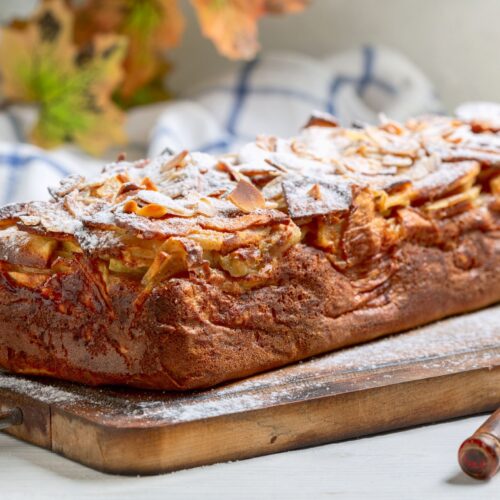 a loaf of apple cake sitting on a wood cutting board
